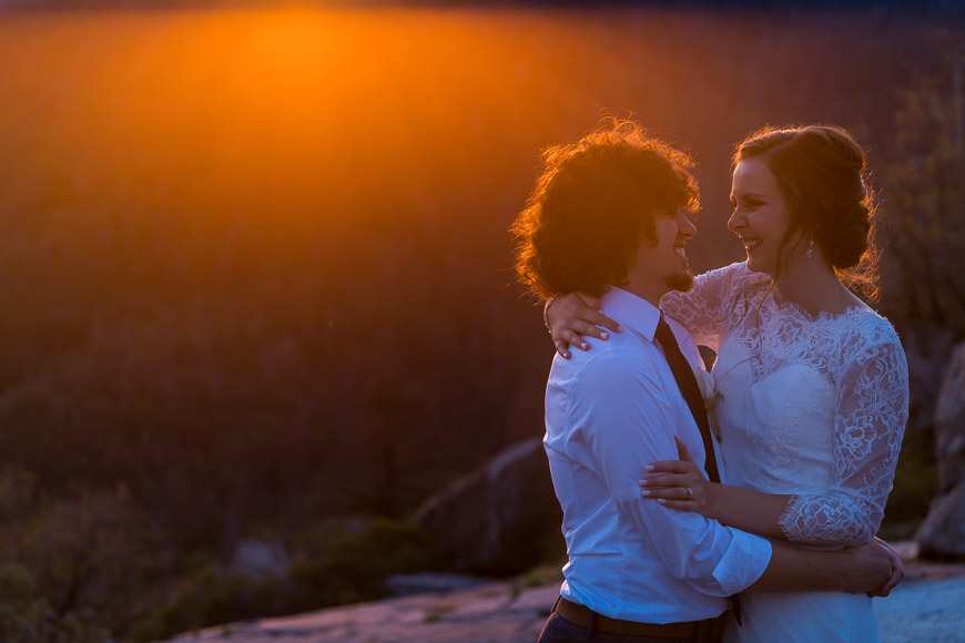 A bride and groom embrace on top of a mountain at sunset.