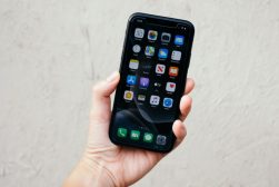 A person holding up an iphone with a screen full of apps.