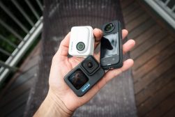 A person holding two action cameras on a deck.