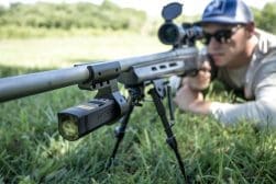 A man leaning on a rifle in the grass.