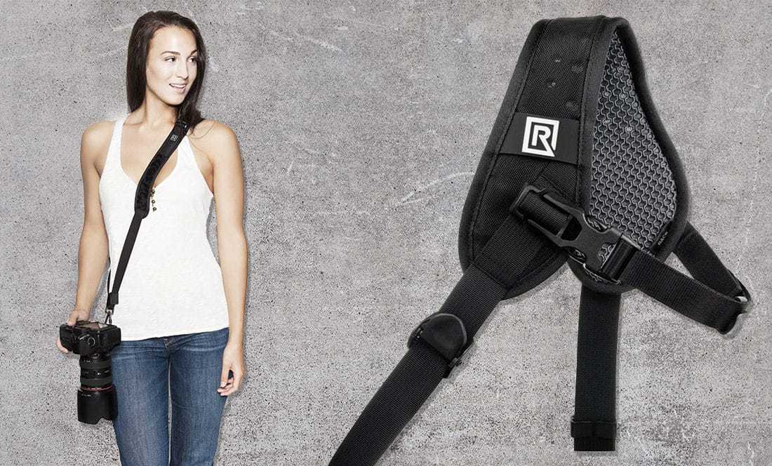 smiling woman in vest and jeans wears camera across her body on a black strap