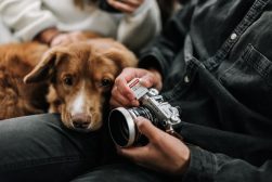 A person holding a camera and a dog.