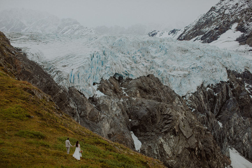 A bride and groom standing on the side of a glacier.