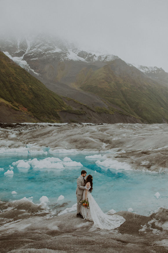 A bride and groom standing on a glacier in alaska.