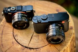 two compact cameras sitting on a wooden stump.