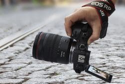 A person holding a camera on a cobblestone street.