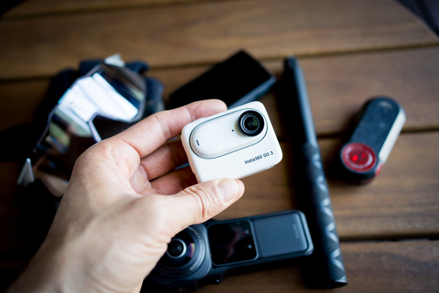 A person holding a small camera and other items on a table.
