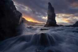 An image of a rock formation in the ocean at sunset.