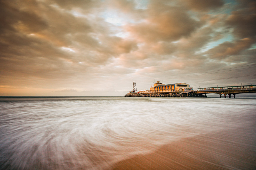 A pier on the beach with a cloudy sky.