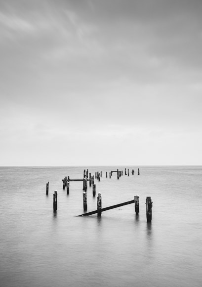 A black and white photo of old wooden posts in the water.