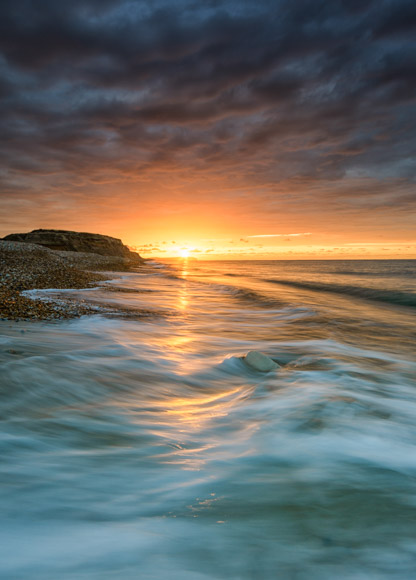 The sun is setting over a beach with waves.