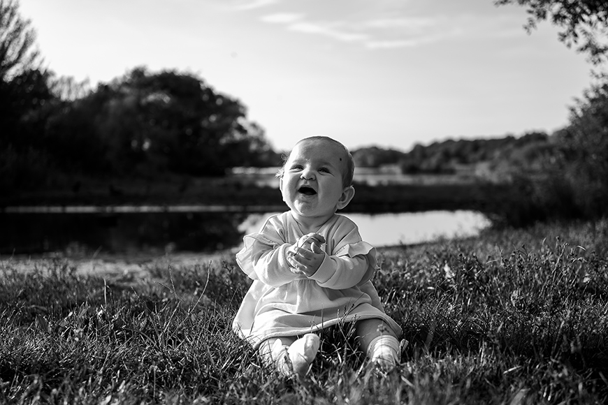 A black and white photo of a baby sitting in the grass.