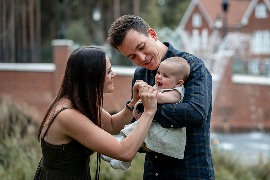 A man and woman holding a baby in front of a fountain.