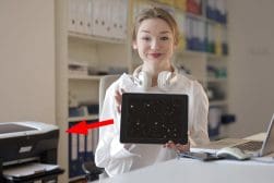 A woman holding an ipad in front of a printer.