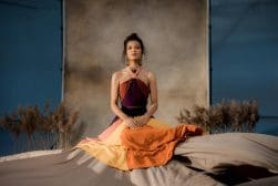 A woman in a colorful dress sitting on a bed.