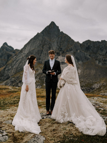 The bride and groom are standing in front of a mountain with mountains in the background.