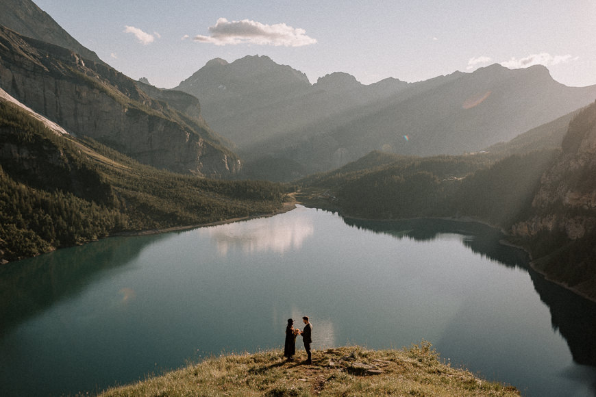 Two people standing on top of a mountain overlooking a lake.