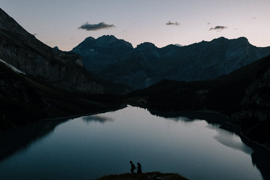 Two people standing on top of a mountain overlooking a lake.