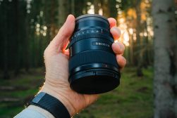 man holding camera lens in front of trees