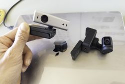 a person holding a webcam next to two other webcams over a Mac laptop.