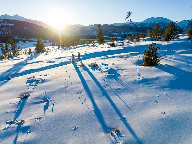 A bride and groom walking in the snow at sunset.