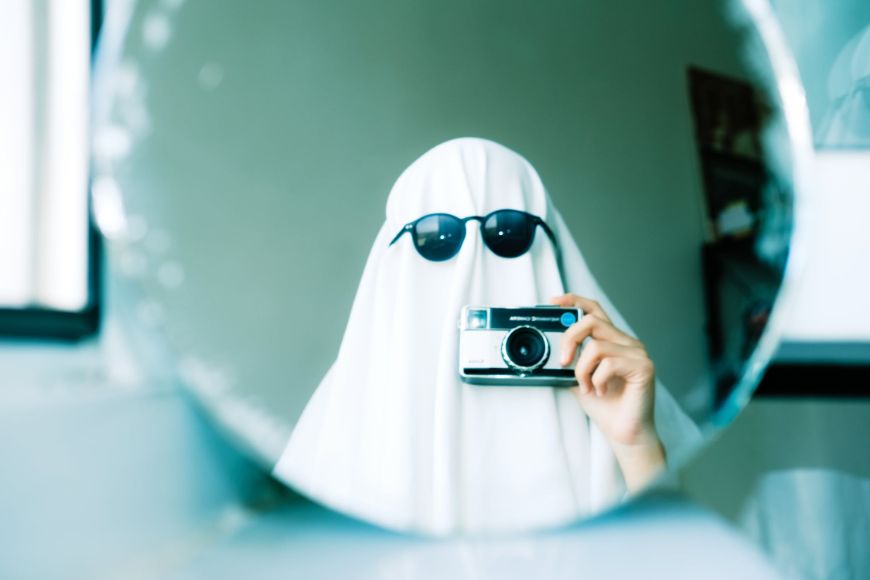 A woman in a white ghost costume taking a photo in a mirror.