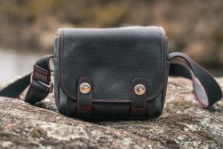A black leather camera bag sitting on top of a rock.