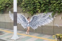 A woman is standing next to a wall with wings painted on it.
