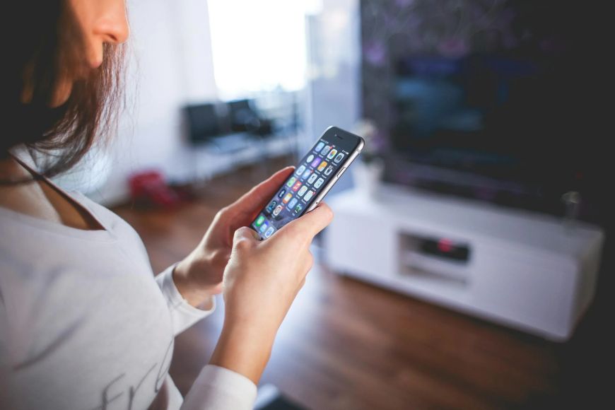 A woman is holding a cell phone in front of a tv.