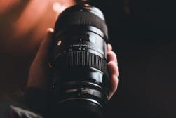 A person holding up a large camera lens.