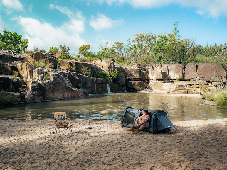 A person sits on a rock next to a body of water.