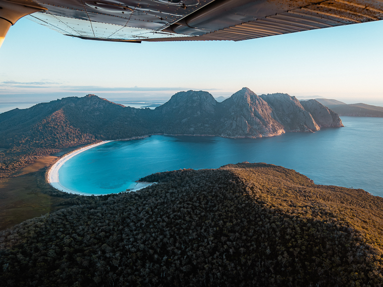 An airplane wing over a body of water and land.