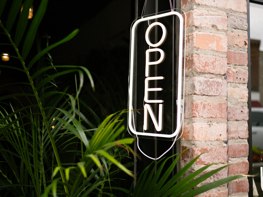 A neon sign with the word open hanging from a brick wall.