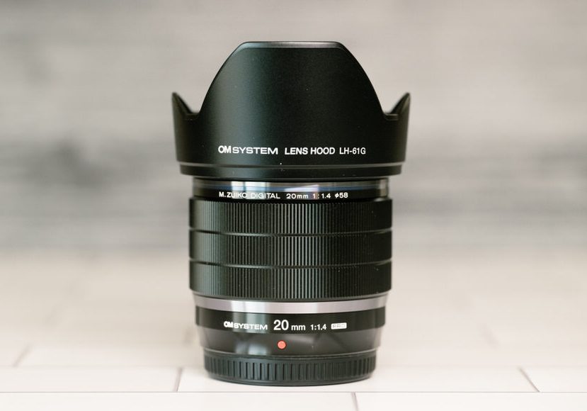 A black lens sitting on top of a tiled floor. The OM System 20mm f/1.4 lens sitting on top of a tiled floor.
