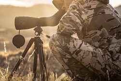 A man in camouflage is looking through a spotting scope.