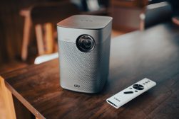 a white projector sitting on top of a wooden table next to a remote.